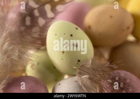 Close-up of pastel coloured, sugar coated mini eggs and feathers Stock Photo