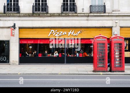 London, UK - March 24, 2024; Central London Pizza Hut restaurant with two red classic telephone phone boxes Stock Photo