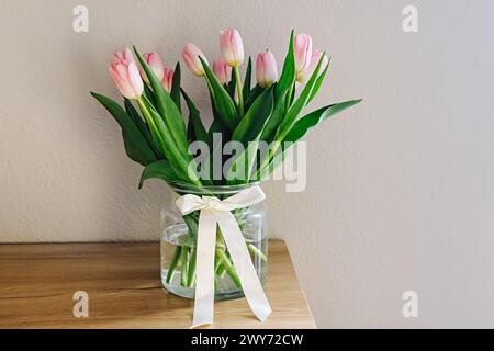 Bouquet of fresh pastel pink tulips in a glass vase decorated with satin ribbon Stock Photo