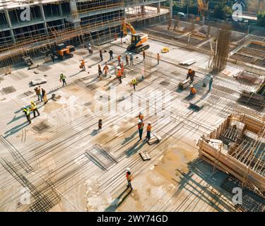 A construction site with a large group of workers in orange vests. Scene is busy and active Stock Photo