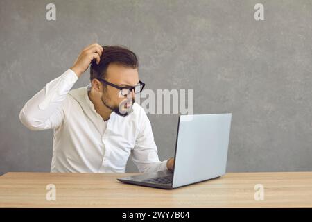 Young man having computer problem and looking at screen of his laptop in confusion Stock Photo