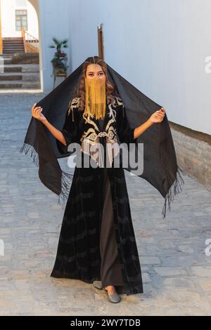 Bukhara, Uzbekistan, Central Asia. August 25, 2021. young Uzbek woman in traditional black dress and gold veil. Stock Photo