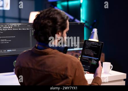 Man doing software quality assurance using tablet, reading source code before implementing it. Programmer inspecting coding on portable device, looking to fix potential bugs Stock Photo