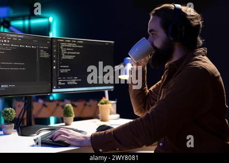 Cybersecurity specialist drinking coffee while looking for company security vulnerabilities and preventing malware infections. Programmer enjoying hot beverage while installing fortified code on PC Stock Photo