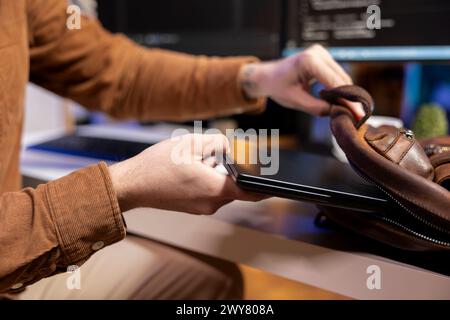 Programmer putting laptop in backpack, leaving office after filtering malicious traffic from cybercriminals attempting to steal company data. Man packing notebook after finishing preventing malware Stock Photo