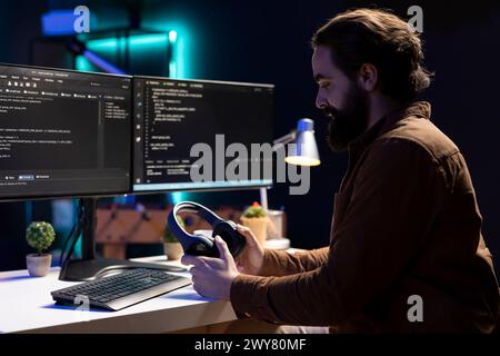 Programmer putting headphones on while implementing security measures to protect company systems and data. IT admin listening music, testing and debugging code for software applications Stock Photo