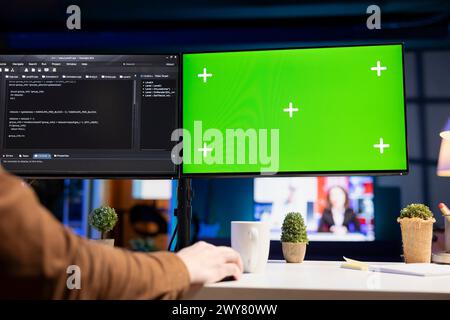 Developer doing software debugging on isolated screen PC at home, checking wrong lines of code displayed on monitors. IT professional in living room fixing coding problems on chroma key computer Stock Photo