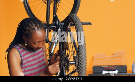 Specialist using screwdriver and hex socket wrench to secure wheel on bicycle in studio background repair shop. Technician screwing bolts on bike parts, fixing rear derailleur, camera A Stock Photo