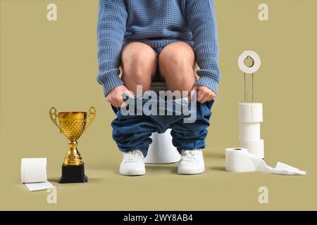 Young man with gold cup sitting on toilet bowl against green background Stock Photo