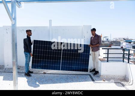 Two indian workers holding solar panel read to instal at roof of house. Green energy, Renewable energy concept, Copy space Stock Photo