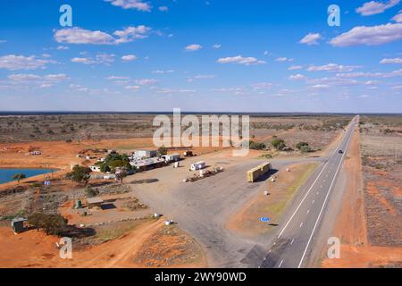 Aerial view of a remote service station with a long straight road across a sparse landscape Stock Photo