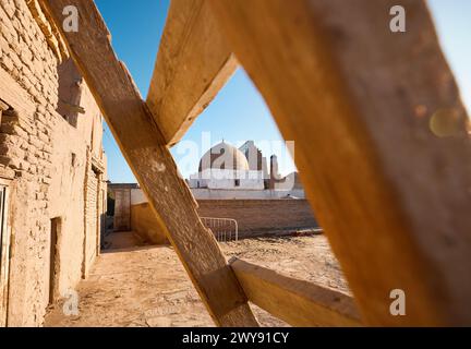 Madrasah and old mosque dome at narrow street with ladder at foreground in ancient city Khiva in Uzbekistan. Stock Photo