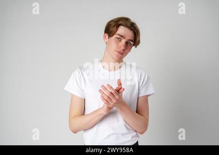 Young Man Clapping Hands in a White T-Shirt Against a Plain Background Stock Photo