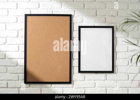 Two Empty Picture Frames Hanging on a White Brick Wall With a Plant in the Foreground Stock Photo
