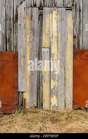 A worn wooden door with flaking yellow paint is framed by rusted metal sheets, conveying decay and neglect. Stock Photo