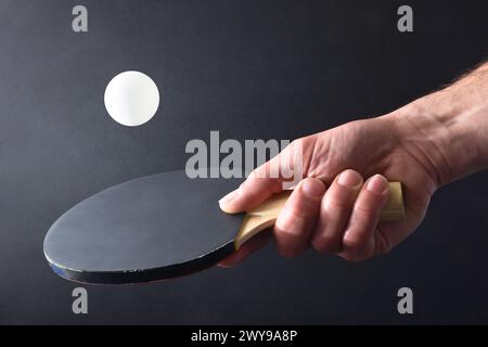 Detail of ping pong player hitting a white ball with the black rubber part of a paddle on black isolated background. Front view. Stock Photo