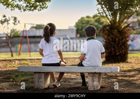 A girl and boy sitting on school playground bench Stock Photo