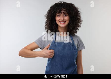 Happy woman wearing kitchen apron and showing thumbs up on light grey background. Mockup for design Stock Photo