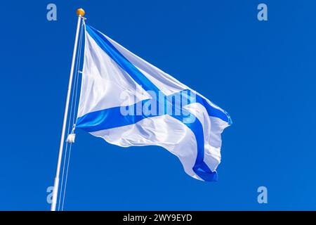 Ensign of the Russian Navy is waving on wind under blue sky, also known as the St. Andrews flag. This is the stern flag of the ships of the Russian Im Stock Photo