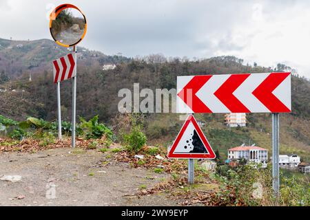 Road signs and convex mirror mounted on a roadside of a mountain road, dangerous turn and Falling rocks Stock Photo