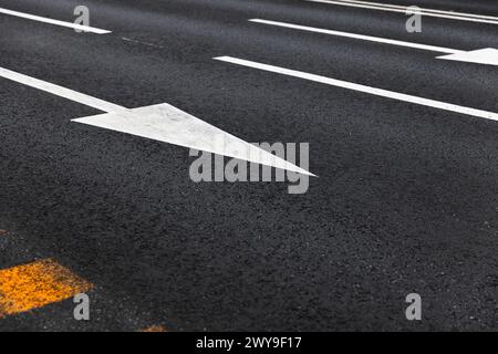 White arrows and lines, road marking on dark highway asphalt. Driving directions by lanes, abstract transportation photo background Stock Photo