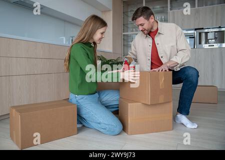 Cheerful couple packing cardboard boxes using sticky tape prepare to move in new apartment together. Stock Photo