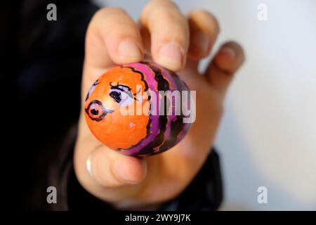 Hand holding a painted hard boiled egg with the face of a fish for use in an Easter egg rolling competition in March 2024 Wales UK  KATHY DEWITT Stock Photo