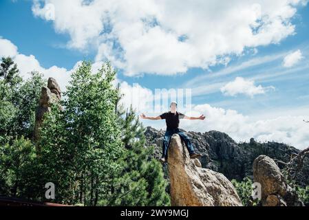 Man with arms outstretched sitting on rocks in sunny mountain scene Stock Photo