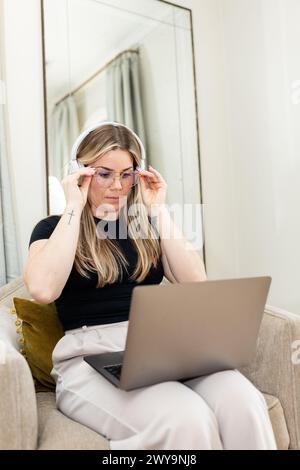 Woman concentrating on laptop work with headphones in a home setting Stock Photo