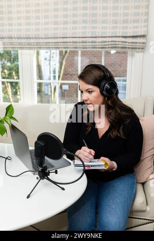 Focused woman podcasting and taking notes at her home recording setup Stock Photo