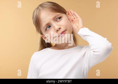 Little girl with hearing problem on pale brown background Stock Photo