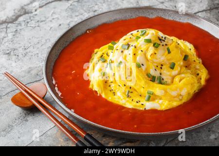 Delicious Asian tornado omelette with sesame seeds, green onions and hot pepper sauce close-up in a plate on the table. Horizontal Stock Photo