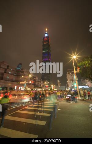 Bustling street scene with moving traffic and pedestrians leads to the illuminated Taipei 101 tower against the dark sky after new year's eve fireworks show Stock Photo