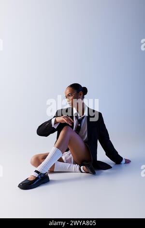 Young African American woman sitting on ground in suit and tie, white studio Stock Photo