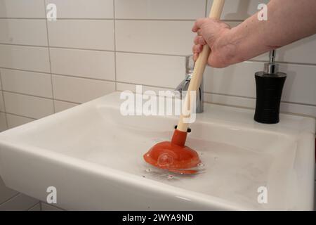 Man using plunger to remove drain pipe blockage on bathroom sink. Just hand and arm of man is seen. Water in sink showing agitation. . Stock Photo