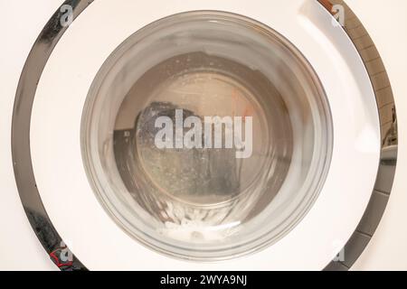 Front view of running washing machine showing distorted foam in turning drum and calcifications on front window from water splling. Stock Photo