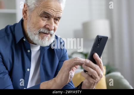 Cheerful elderly man enjoys browsing on his phone, exuding happiness and ease in a comfortable domestic setting. Stock Photo