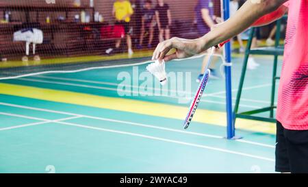 The badminton player holding a white shuttlecock and racket and standing at the net ready to serve. Stock Photo