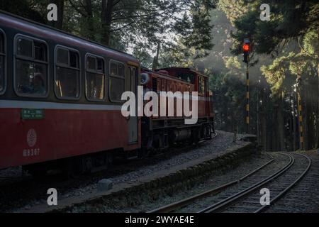 An old-fashioned train travels on a curved railway track through misty woods with light beams piercing through the forest in Alishan National Park Stock Photo