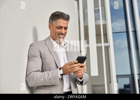 Smiling middle aged business man standing outdoors using mobile phone. Stock Photo