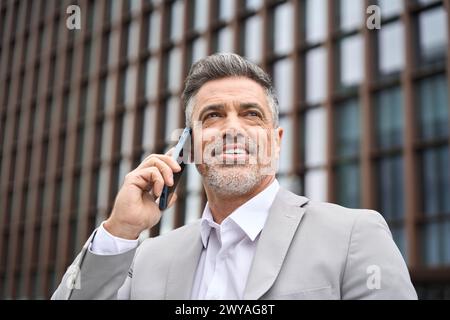 Busy mid aged business man making call talking on phone standing on city street. Stock Photo