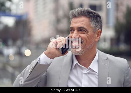 Busy happy middle aged business man making call talking on phone on city street. Stock Photo