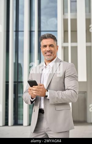 Confident mature business man outdoors using cell phone, vertical portrait. Stock Photo