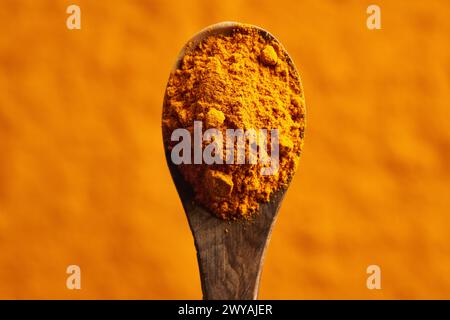 Ground turmeric root powder on a wooden spoon over orange background with copy space, top view Stock Photo