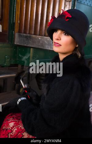 Attractive young woman in red 1920s flapper dress and cloche hat travelling by antique steam train Stock Photo