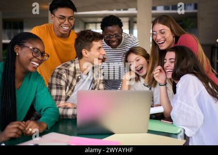 Group of young diverse students people laughing using laptop in the cafeteria on university campus Stock Photo