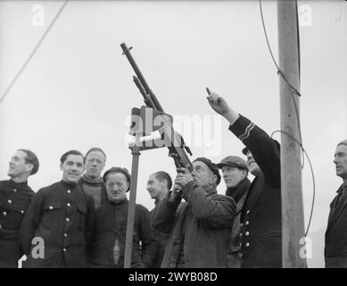 MOBILE DEMS INSTRUCTIONAL YACHT. 23 FEBRUARY 1942, ON BOARD THE MY MELITA, GOUROCK BAY. THE MOTOR LAUNCH IS THE FIRST INSTRUCTIONAL LAUNCH TO BE USED FOR THE DEFENSIVE EQUIPMENT OF MERCHANT SHIPS IN THE UNITED KINGDOM. SHE MAKES DAILY JOURNEYS TO THE ANCHORAGES TO KEEP THE MERCHANT SEAMEN INFORMED AND INSTRUCTED IN THE LATEST IMPROVEMENTS FOR THE DEFENCE OF THEIR SHIPS. - Merchant seamen being instructed in the use of a Hotchkiss machine gun mounted on the MELITA. , Stock Photo