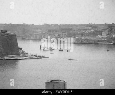 BOMB DAMAGE IN MALTA AFTER BIGGEST RAID YET. 7 APRIL 1942. BOMB DAMAGE TO THE DOCKYARDS. - All that is left of the 200 ton Floating crane in the dockyard after direct hit from a bomb. In the background can be seen the supply vessel PLUMLEAF with a heavy list after being hit. , Stock Photo