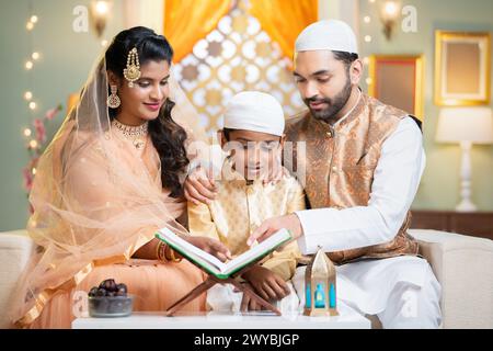 Indian muslim parents helping kid to reading quran before fasting food during ramadan festival at home - concept of festival ,supportive family and Stock Photo