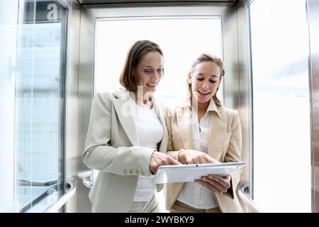 Two executives in elevator, using a digital tablet. Stock Photo
